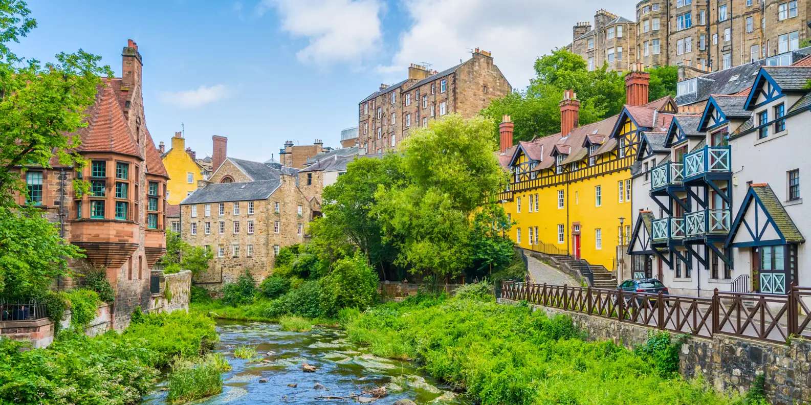 Picturesque Dean Village in Edinburgh with colorful historic buildings including bright yellow and timber-framed houses along Water of Leith river.