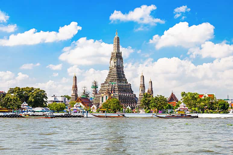鄭王廟(Wat Arun)的華麗尖塔以彩色瓷磚裝飾,高聳於湄南河之上。藍天白雲映襯下,傳統泰國建築與水面船隻相映成趣。